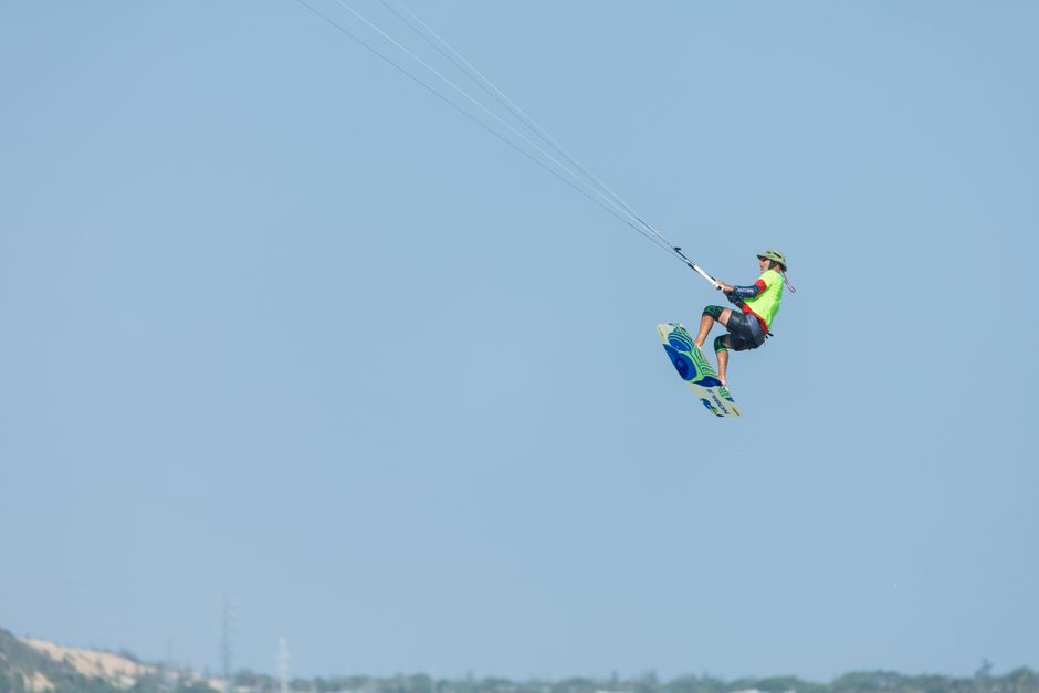 A thrilling shot of a kitesurfer performing a midair jump against a bright blue sky.