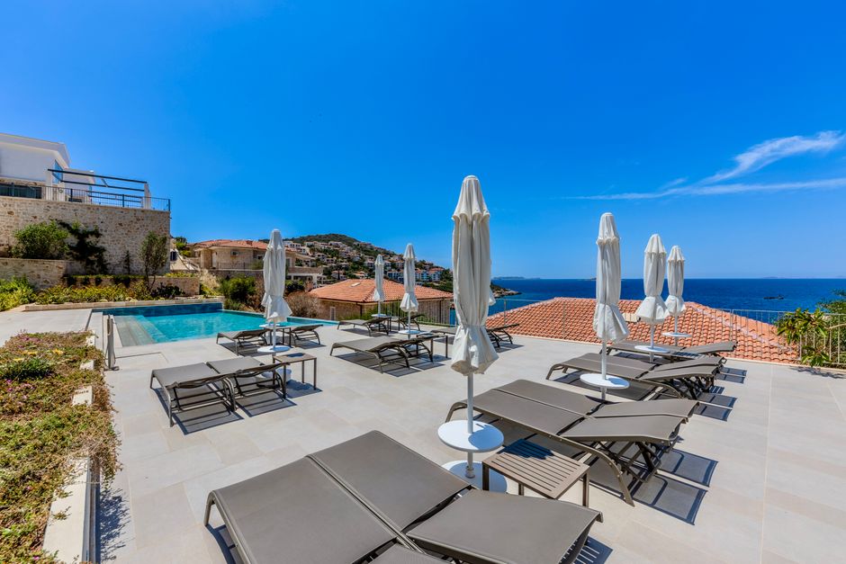 Relax by the luxurious pool with sun loungers and umbrellas, overlooking the sea and beautiful coastal landscape.
