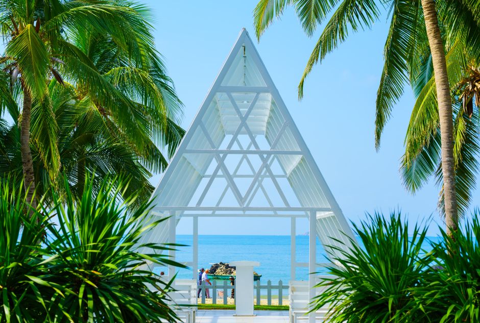 A serene tropical beachfront with a modern A-frame chapel surrounded by palm trees, perfect for weddings.