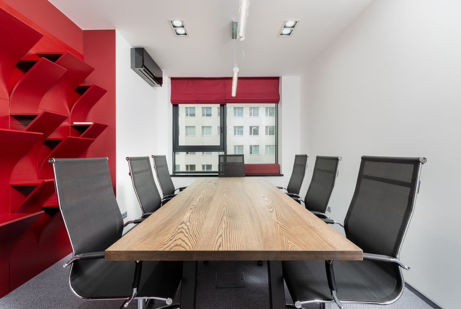 Interior of modern conference room with wooden table and chairs next to red shelves near window with jalousie
