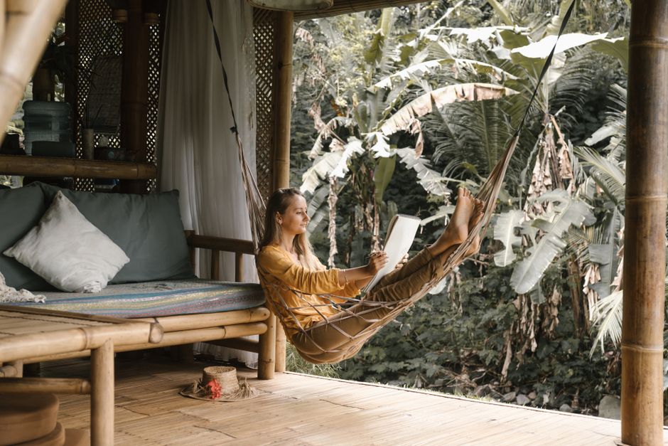 Woman enjoying relaxation on a bamboo porch, reading in a hammock surrounded by tropical greenery.