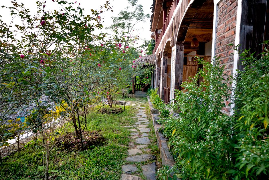 Narrow pathway between green plants and stone house with terrace in tropical countryside