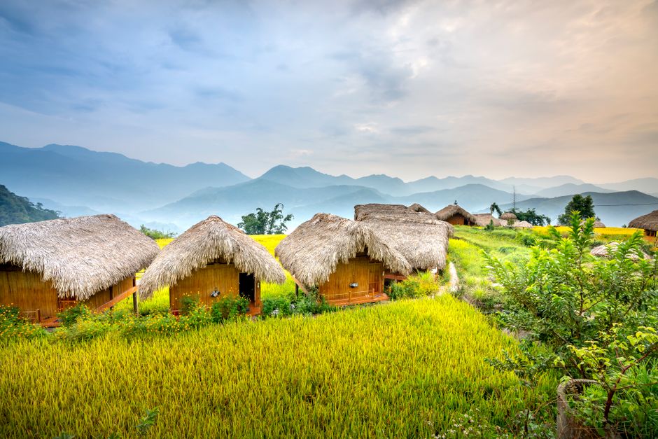 Small village with houses on green grass near hills and trees under bright sky in daytime