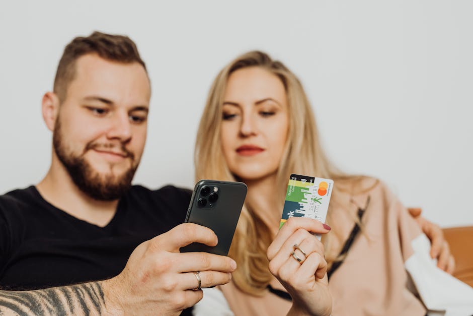 A couple shopping online together using a smartphone and credit card while sitting comfortably indoors.