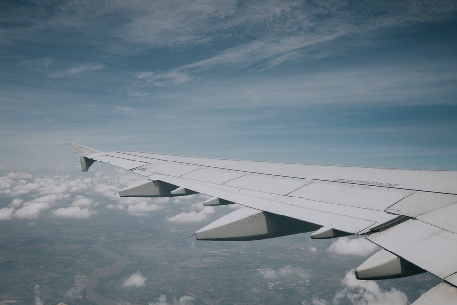 Aerial view from airplane window showing wing and clouds beneath a clear blue sky.