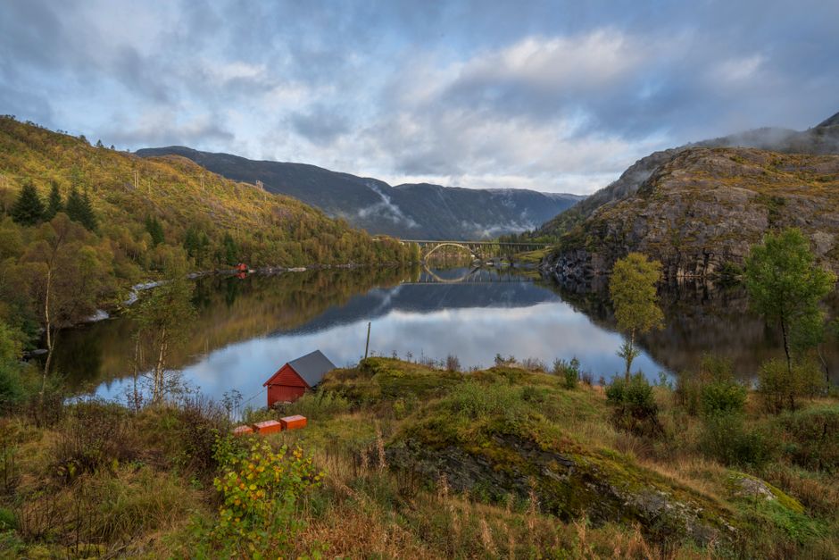 Scenic view of a tranquil lake reflecting mountains and a bridge in Norway.