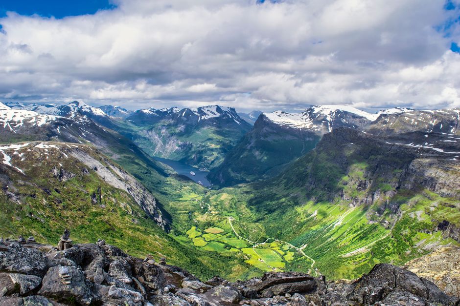 Stunning panoramic view of a lush valley surrounded by snow-capped mountains under a vibrant sky.
