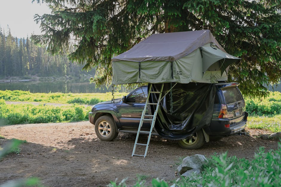 A car equipped with a rooftop tent is parked in a serene forest campsite by the lake.