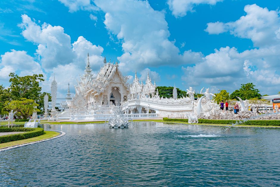 The iconic White Temple in Thailand captured on a sunny day with clear reflections.