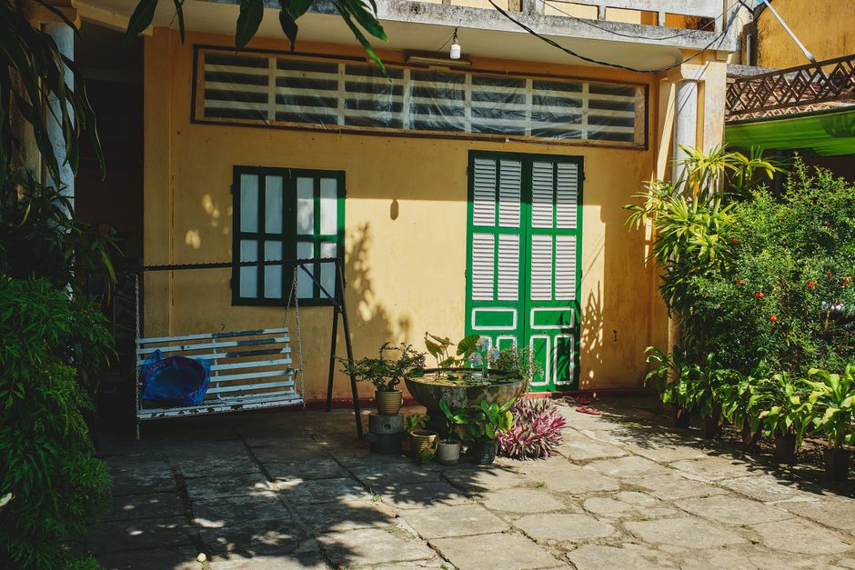 A serene courtyard in Hội An, Vietnam, featuring plants, a swing, and sunlight casting shadows on yellow walls.