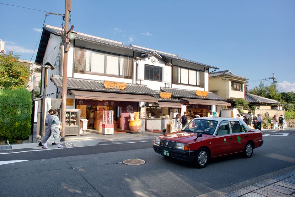A vibrant street scene in Kyoto, Japan, featuring a red taxi and traditional architecture.