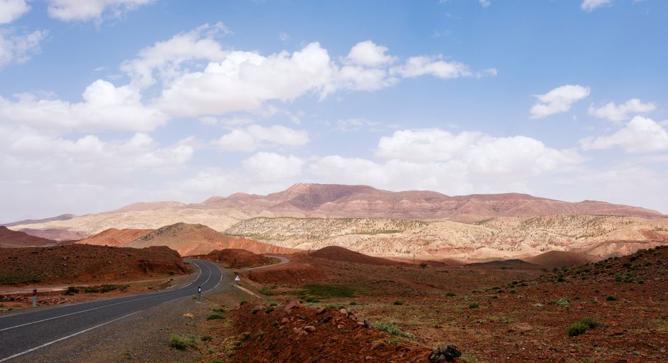 A picturesque curving road through the rugged Atlas Mountains under a vivid blue sky in Morocco.