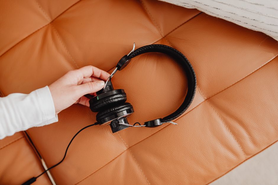 Close-up of a hand holding black headphones on a brown leather couch, emphasizing music and technology.
