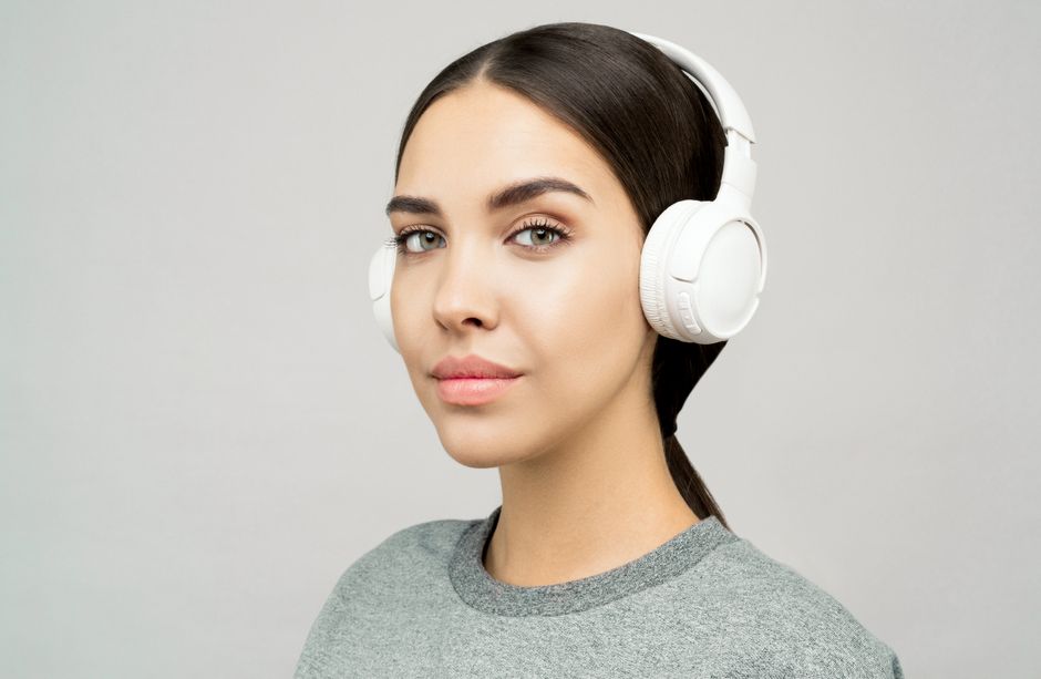 Young woman wearing headphones, posing in a studio setting with a gray background.