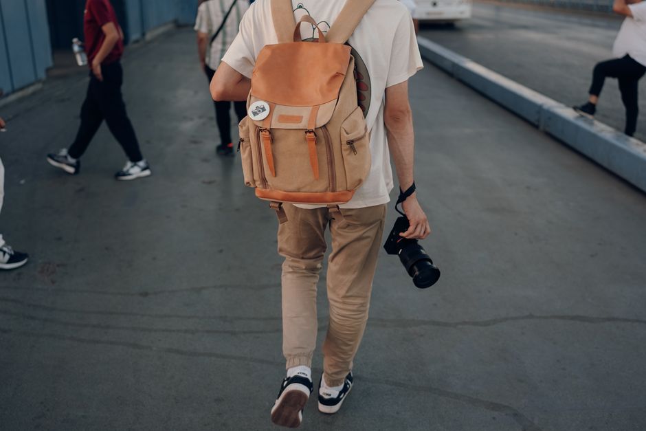 Backpacker holding camera walking in city street, ideal for travel and lifestyle imagery.