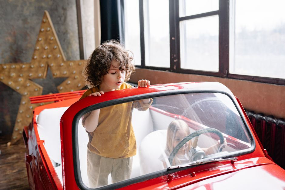 Two children enjoying a playtime adventure in a red toy car in an indoor setting.