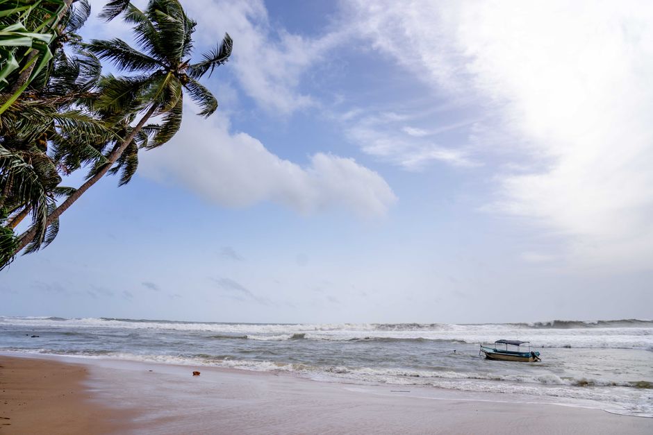 A tranquil beach scene with palm trees, gentle waves, and a boat near the shore.