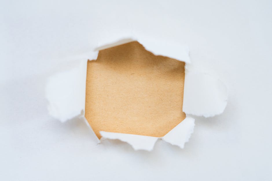 Close-up of torn white paper revealing a blank brown surface underneath.