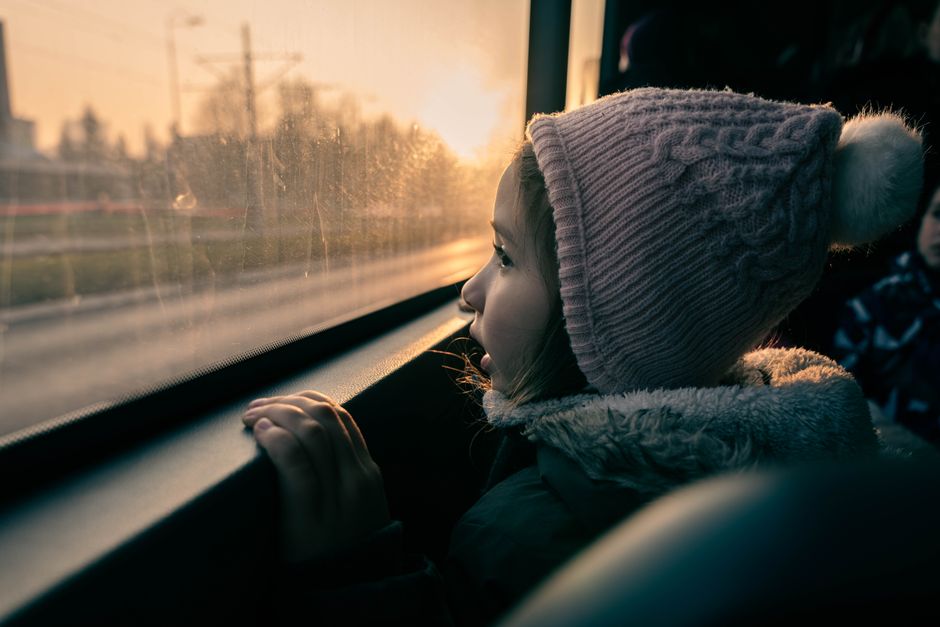 A young girl in Sarajevo gazes out the bus window during sunset, capturing a serene moment.
