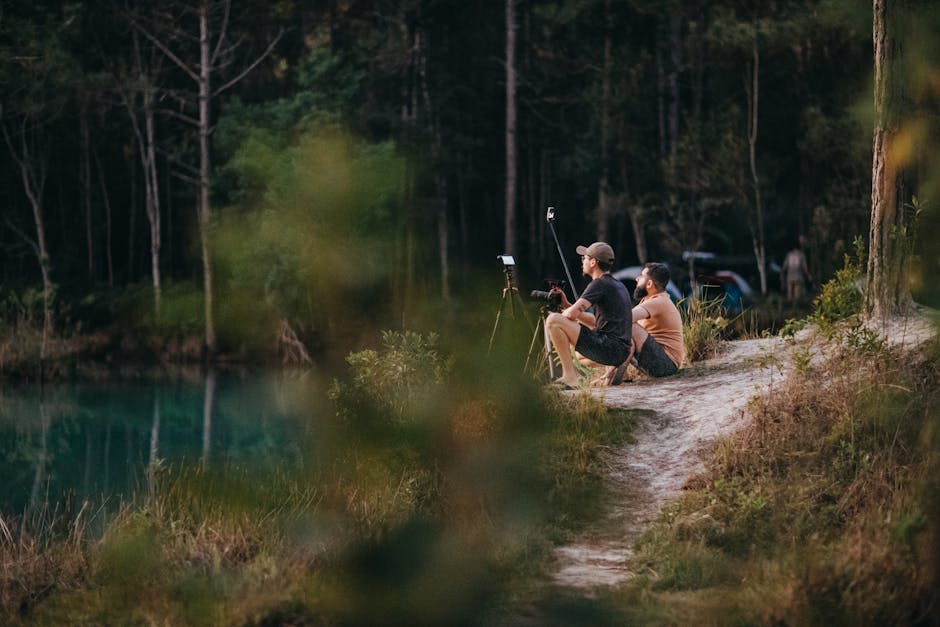 Two men enjoy a peaceful moment by a forest lake, capturing nature on camera.