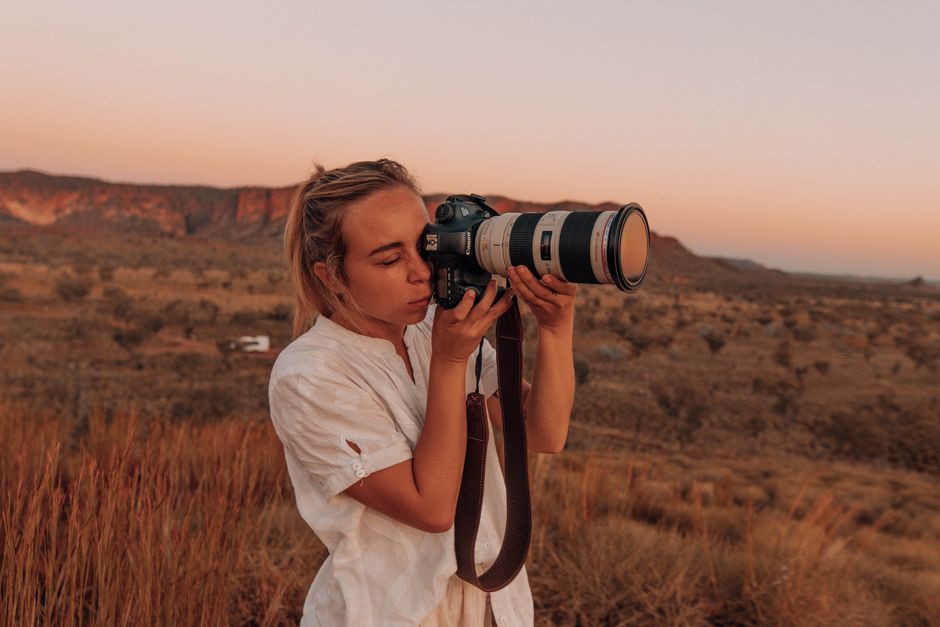A woman photographer using a camera at sunset in a desert landscape. Perfect for travel and lifestyle themes.