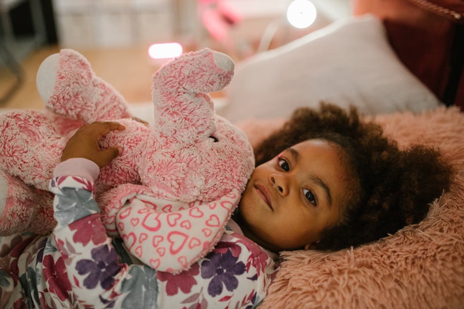 Adorable child hugging a pink plush elephant toy on bed indoors.
