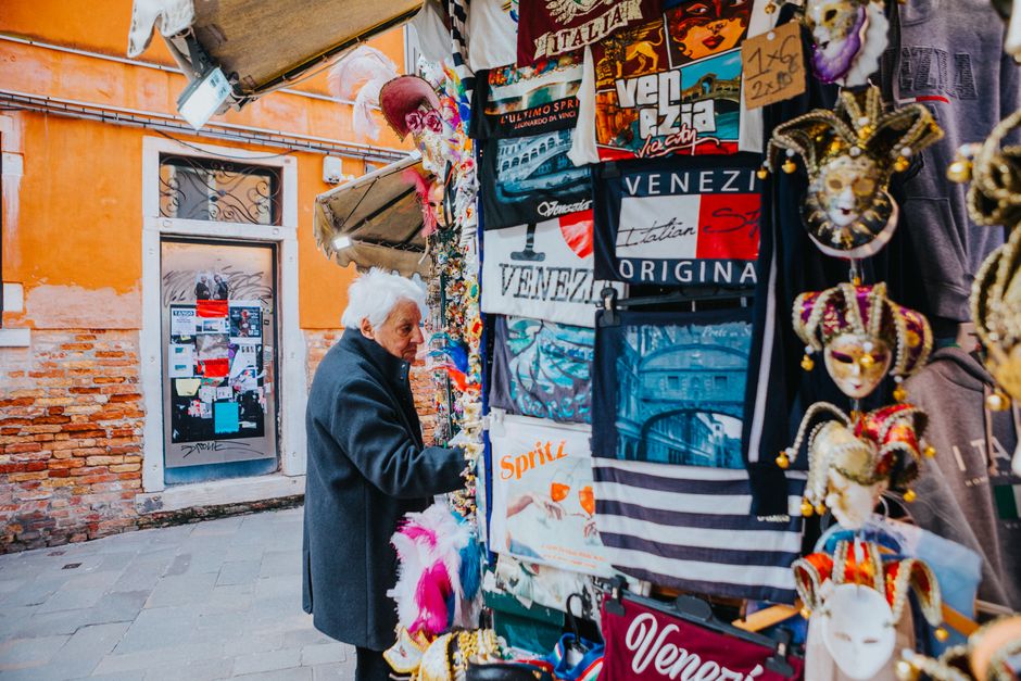 Colorful Venetian souvenir stall with masks and t-shirts in a bustling street market.