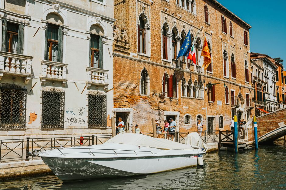 A vibrant view of a canal in Venice with historic architecture and a moored boat under a sunny sky.